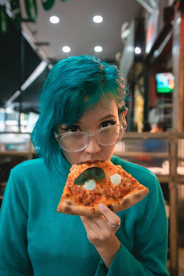 Woman with Green Hair Eating Pizza | Photo by Athena Sandrini