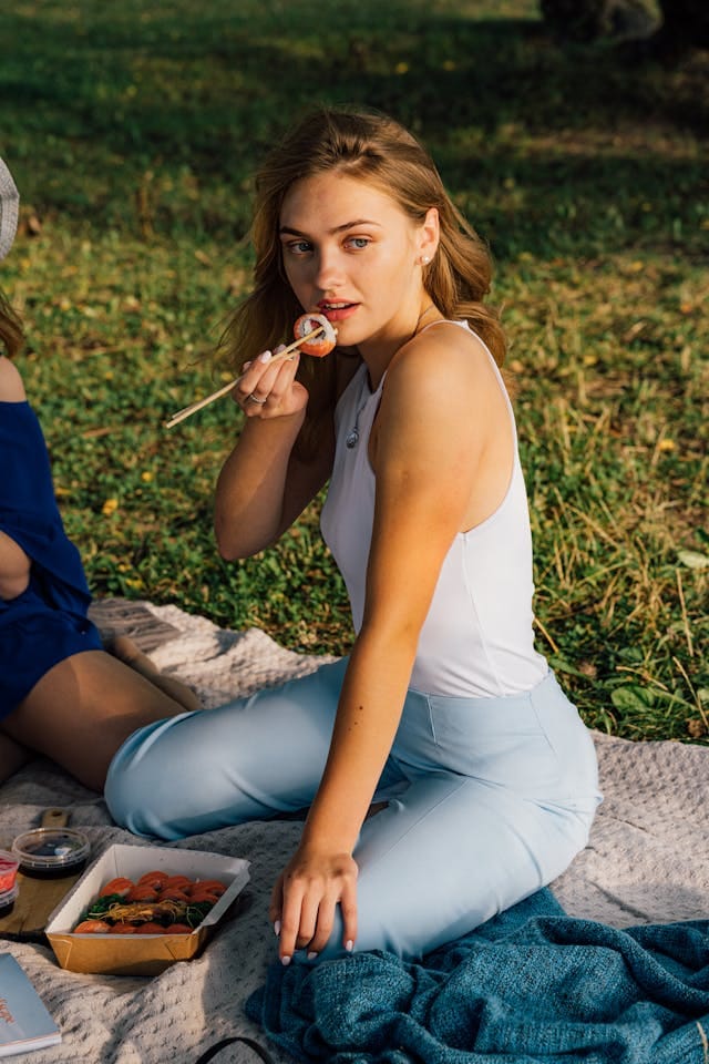 Woman in White Tank Top and Blue Pants Eating Sushi | Photo by Antoni Shkraba